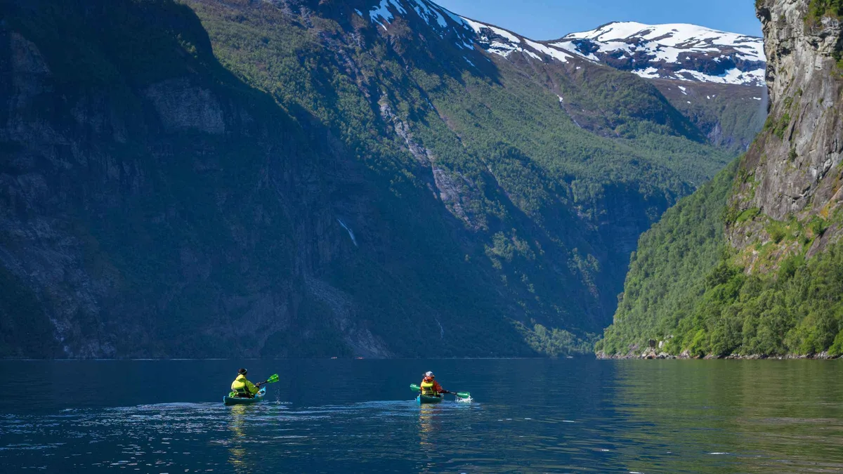 Tandem kayaks paddling beneath waterfalls on a Geiranger fjord cruise alternative kayak tour in Norway